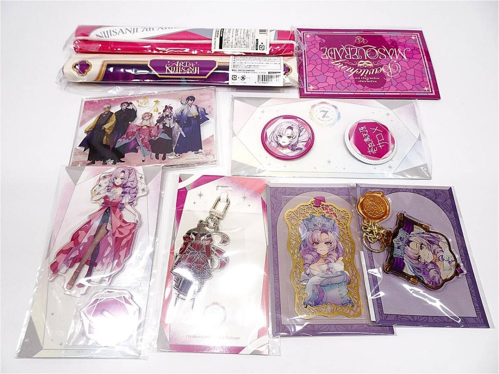 02 1 | Vtuberグッズ買取専門店 Assorted anime merchandise on a white surface: character art cards, stickers, and a pink-purple keychain set in packaging.