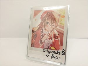Anime-style illustration of a girl with glasses in a red school uniform, framed and resting on a white surface, signature at the bottom.