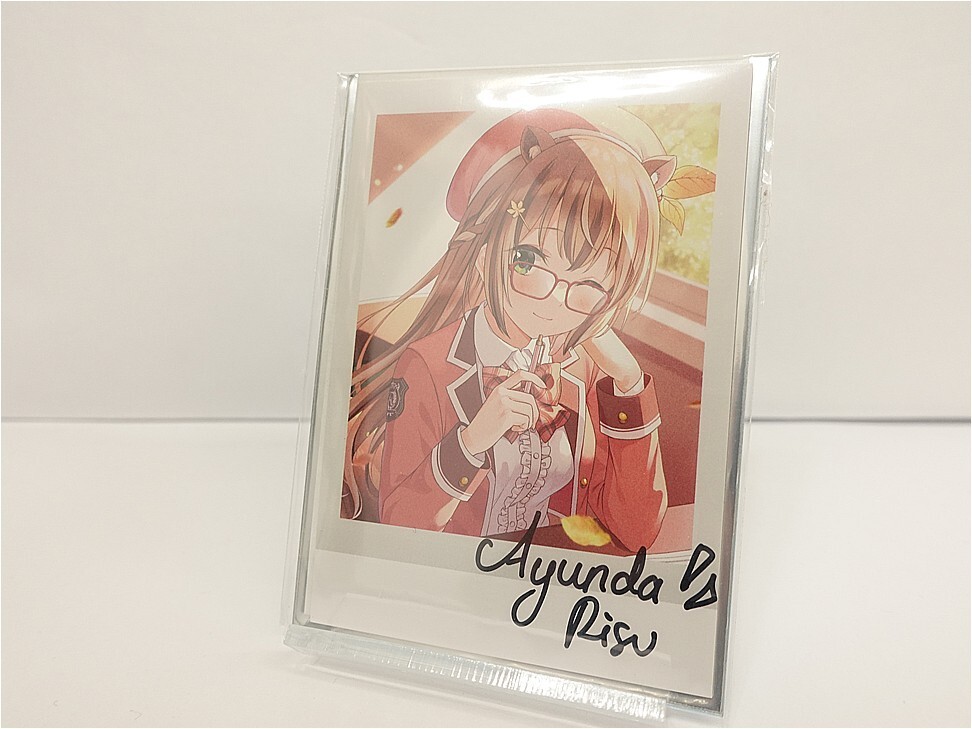 Anime-style illustration of a girl with glasses in a red school uniform, framed and resting on a white surface, signature at the bottom.