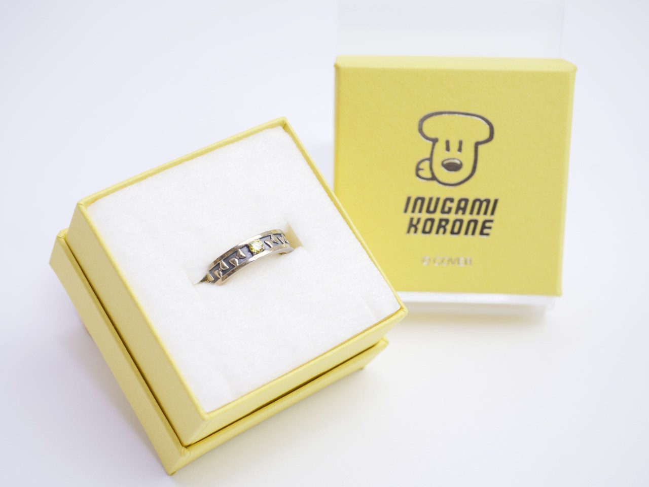 Silver ring with a cutout pattern rests in white foam inside a pale yellow jewelry box.