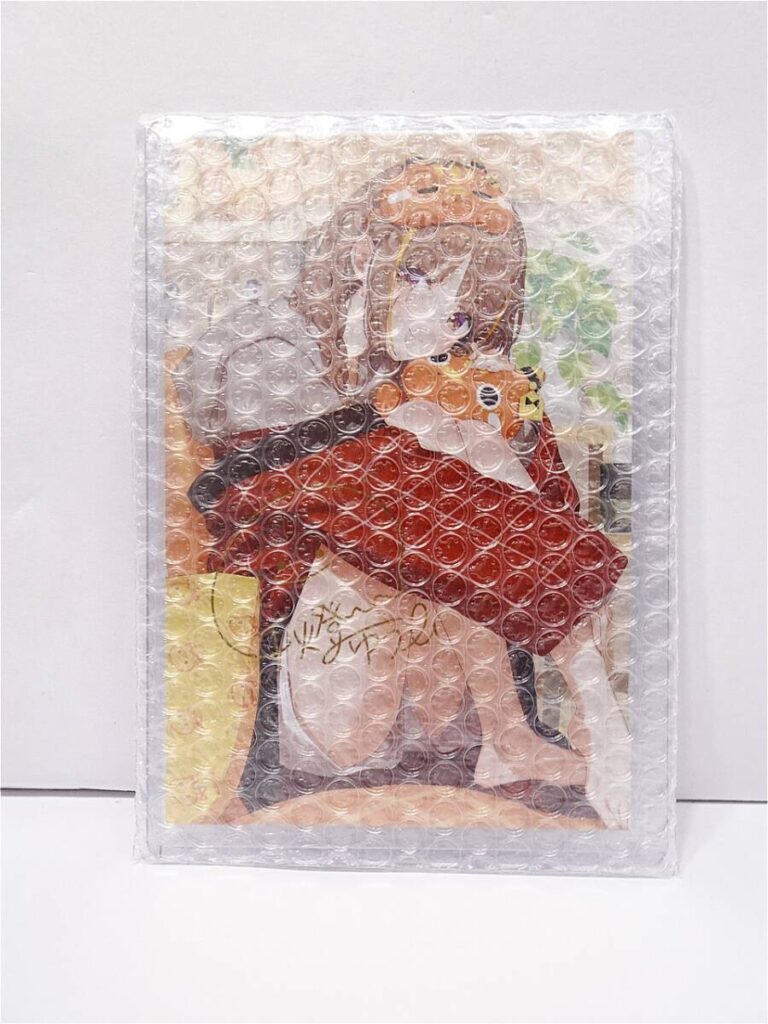 d12047671421 1 | Vtuberグッズ買取専門店 Illustrated art print of a girl with orange hair wearing a red dress, visible through bubble wrap for packaging.