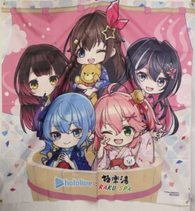Five chibi-style anime girls in a hot-spring tub with a teddy bear, on a pink banner that reads hololive and RAKU SPA with confetti in the background