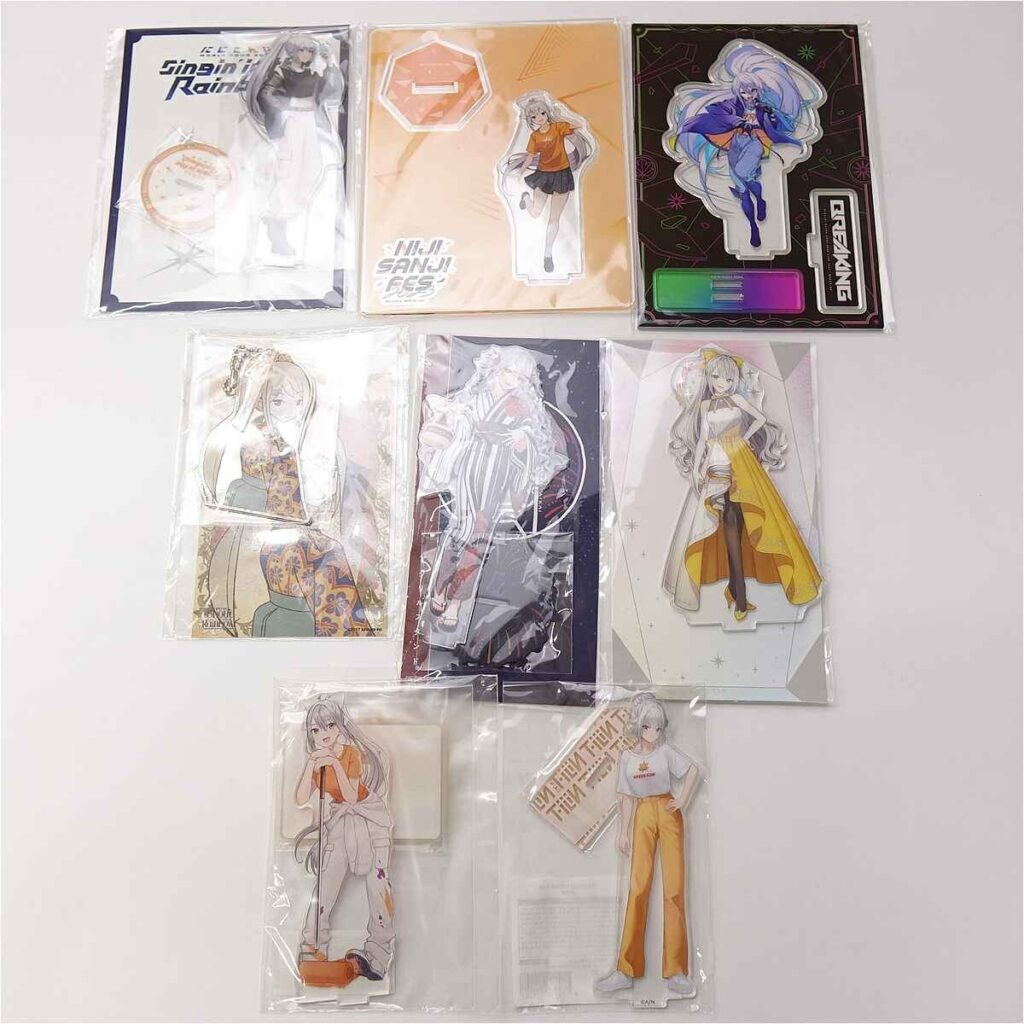 Assorted anime standee cutouts in plastic sleeves laid out on a white surface, showing colorful character poses and outfits.