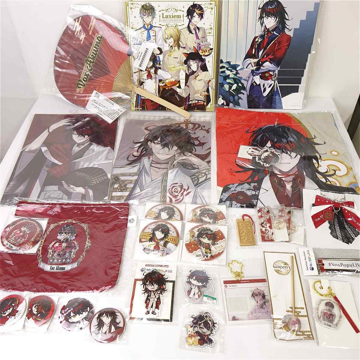 Table full of anime merchandise: posters, clear files, a red tote bag with a character, pins, stickers, and keychains featuring stylized male characters.