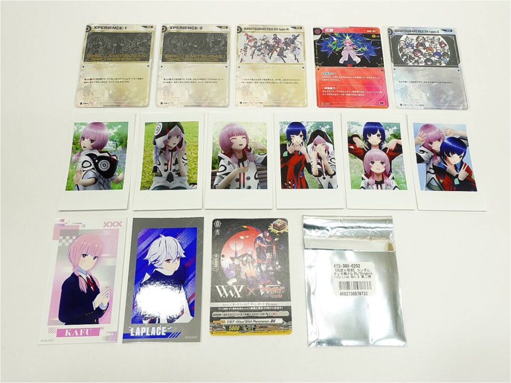 Row of collectible anime trading cards on a white surface, including foil cards on top and character photo cards below.