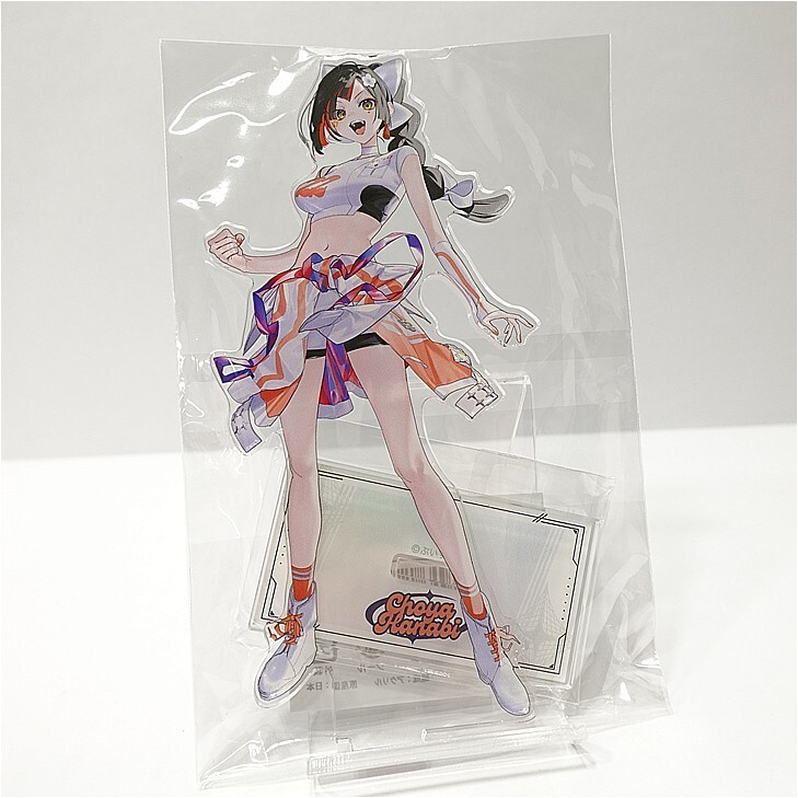 Anime-style female character standee in plastic packaging, wearing a cropped top, colorful skirt, and sneakers; posed as a dynamic figure.
