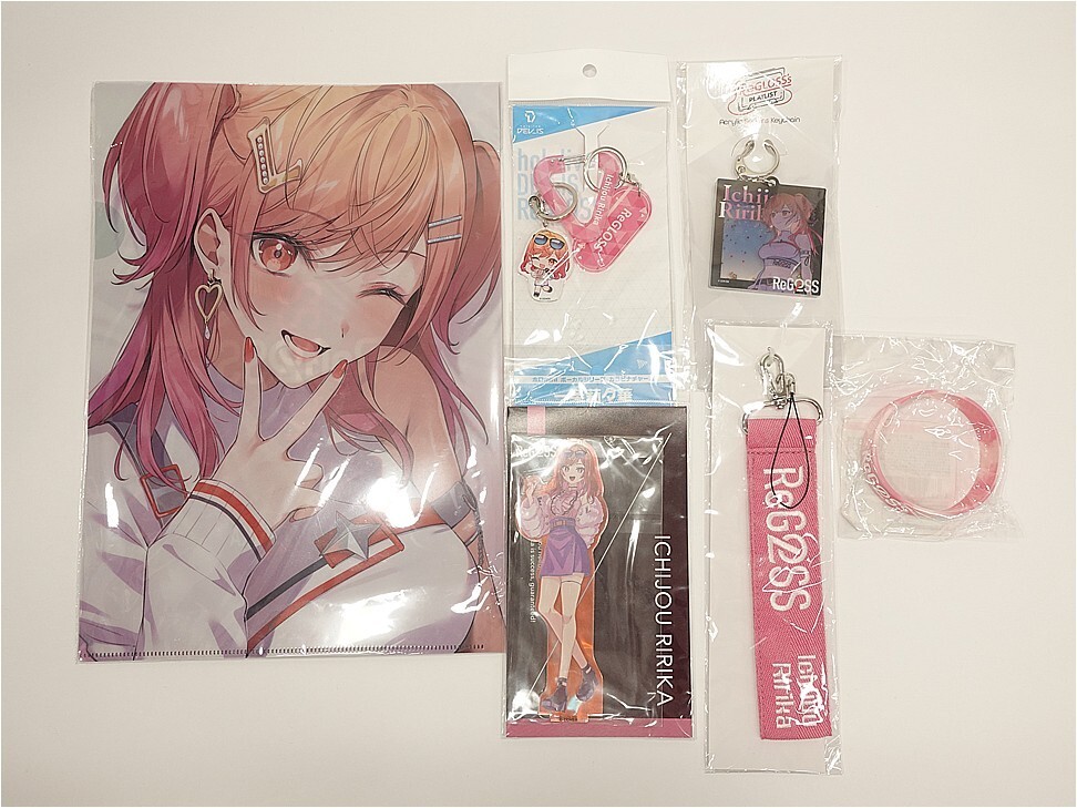 Poster of a smiling pink-haired anime girl with various merch laid out: keychains, pins, a lanyard, a pink wristband, and tape on a white surface.
