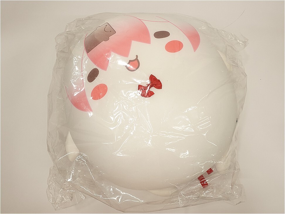 Round white plush pillow with a pink cartoon face and red bow, wrapped in clear plastic wrap.