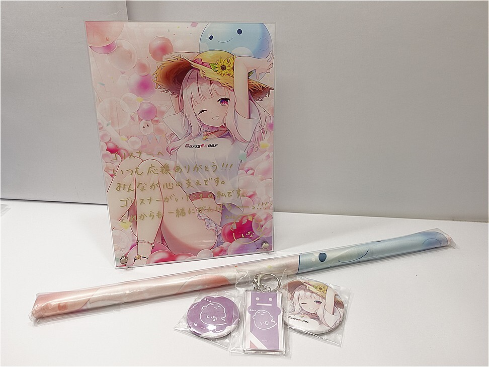 Merchandise layout: large anime poster of a girl with balloons, plus a pastel blue rolled item and a light pink poster tube on a white table.
