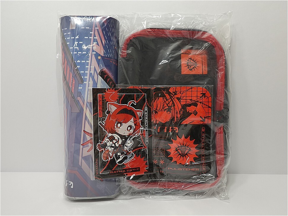 Bag set in clear plastic wrap showing a red-trim backpack and related anime artwork cards inside