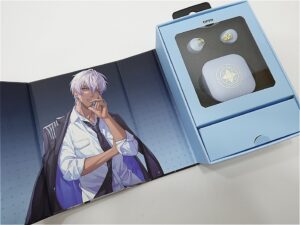 Blue open-box packaging showing wireless earbuds and charging case with a star emblem; the box sits on an anime-style illustration.