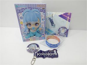 Blue-haired chibi figure box from Hololive with accompanying accessories laid out: a blue wristband, round pin, metal keychain, and a holographic-looking badge/sticker, all on a white surface.