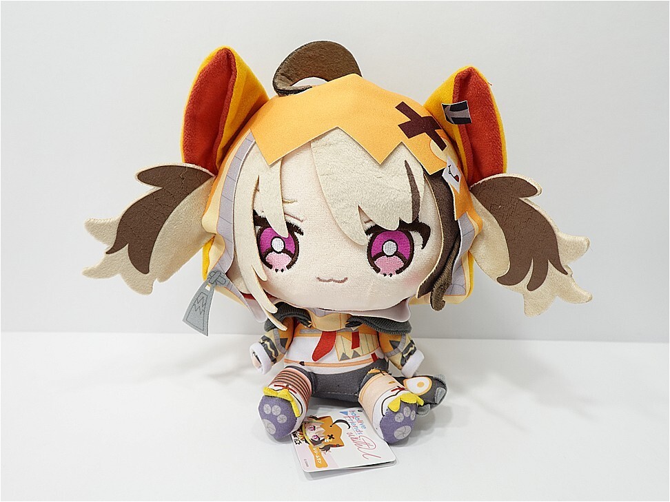 Chibi plush toy of a character with orange hood and pink eyes, sitting on a white surface with a small tag nearby.