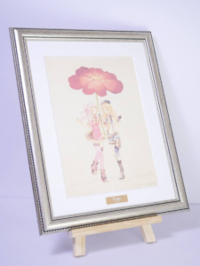 image | Vtuberグッズ買取専門店 Framed illustration of two anime-style girls holding a large pink flower on a wooden easel.