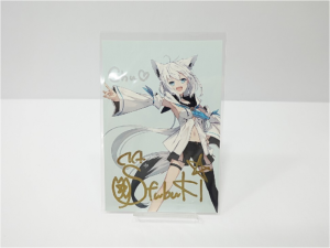 image | Vtuberグッズ買取専門店 Signed illustrated card featuring a white-haired anime character with cat ears, pointing forward in a light outfit and gold signature text at the bottom.