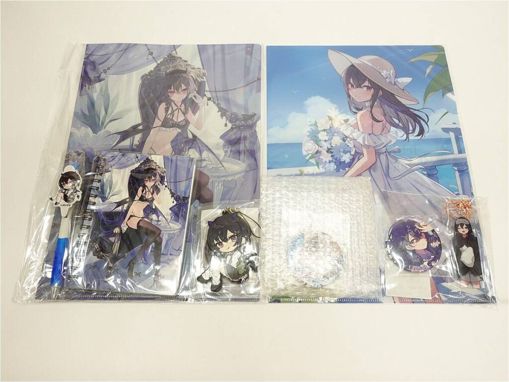 Collection of anime merchandise laid out on a white surface: two large posters of a dark-haired girl, plus notebooks, acrylic standees, keychains, and pins featuring the same character.