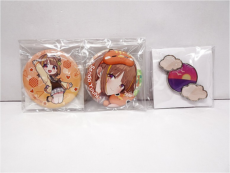v12038018661 1 | Vtuberグッズ買取専門店 Three anime-themed pin badges in plastic bags lined up on a white surface (two round character designs and one cloud-sunset pin).